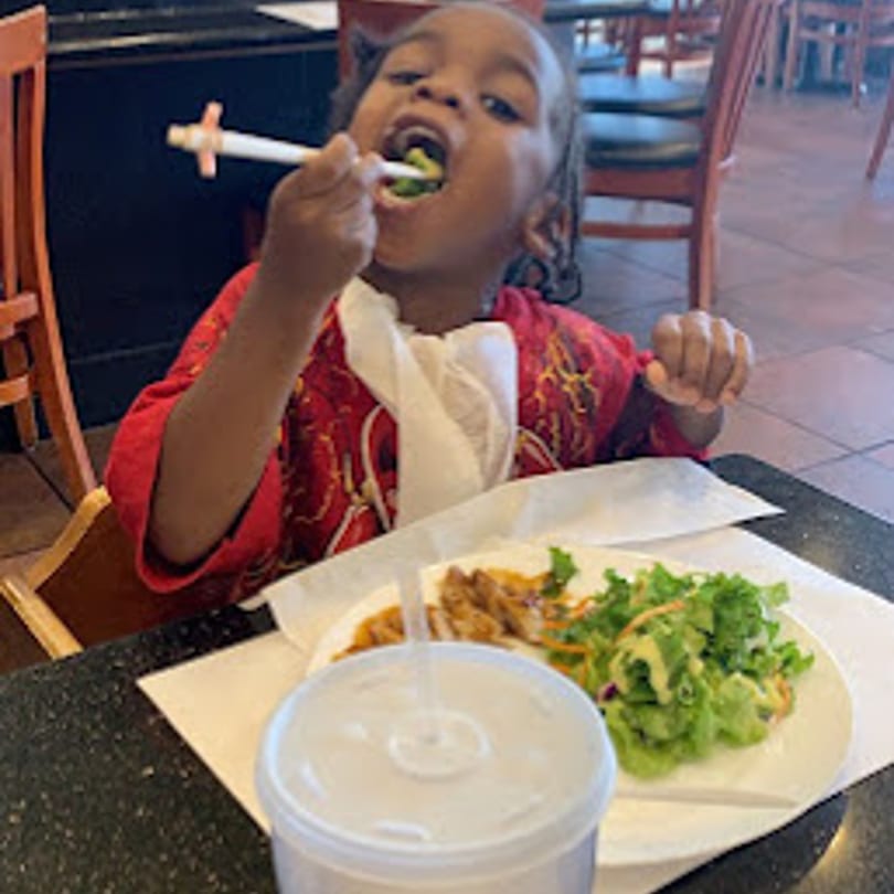 A child in a red shirt happily eats a salad with chopsticks at Yoshi Japanese Cuisine.
