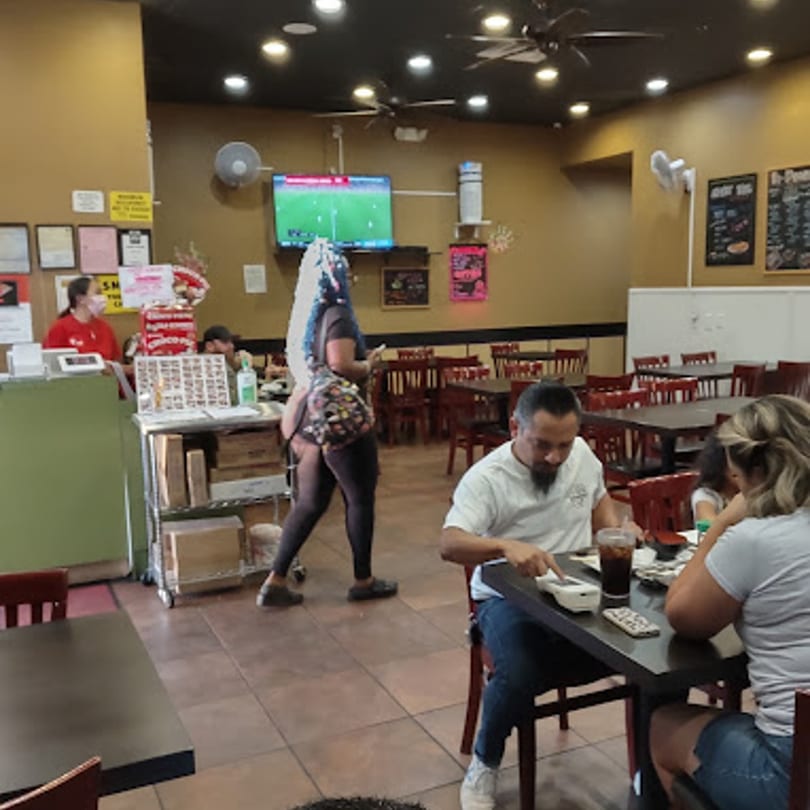 Diners eating at tables in Yoshi Japanese Cuisine, with a TV showing sports in the background.